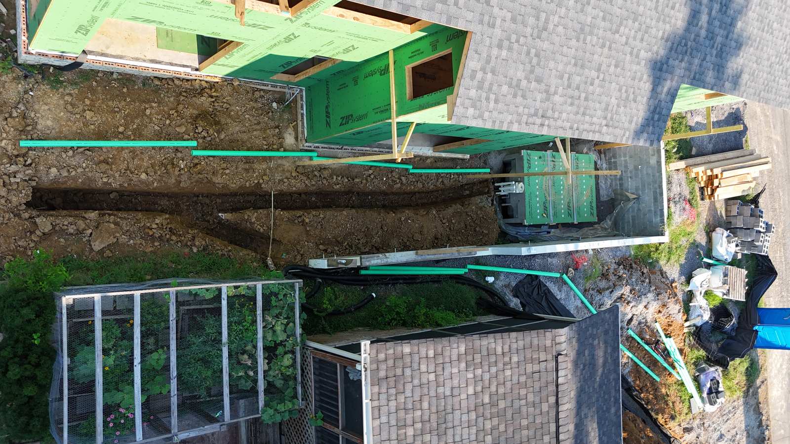 Aerial of a utility trench between a ZIP-sheathed house and a neighbor.