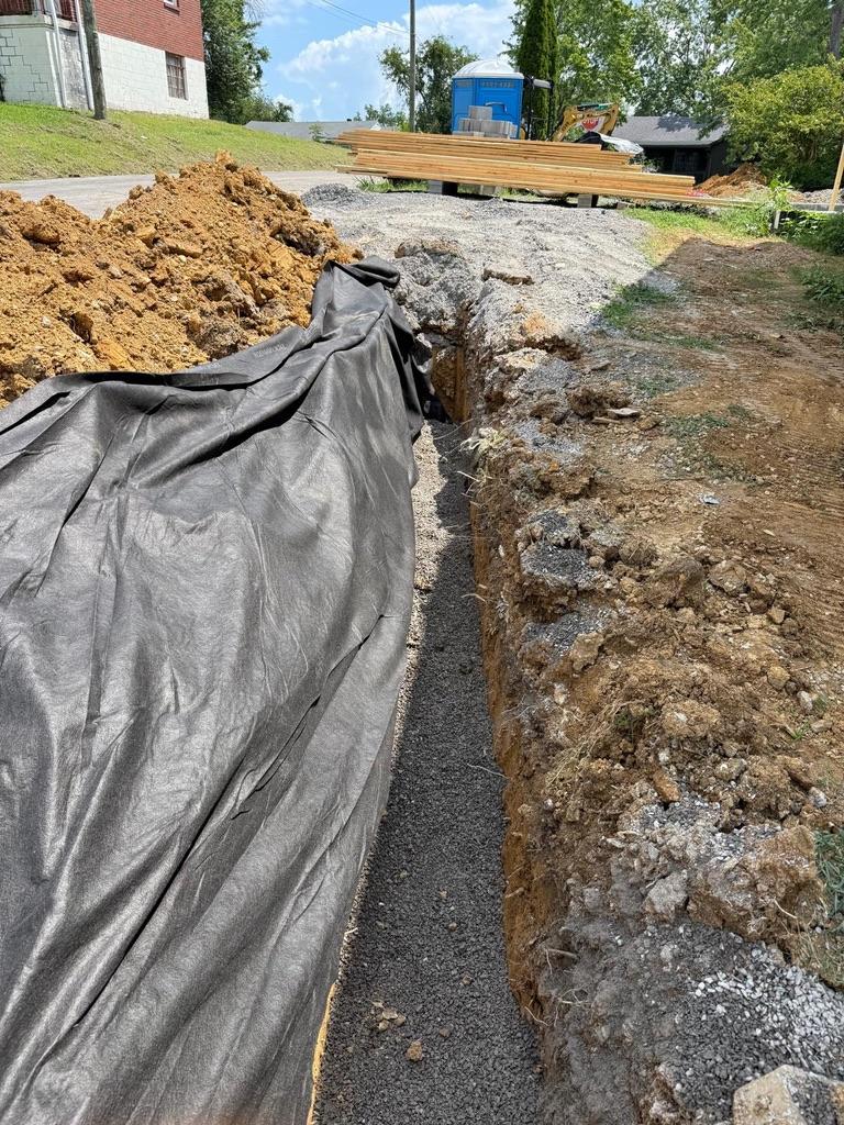 Open drainage trench with geotextile fabric and gravel bedding.