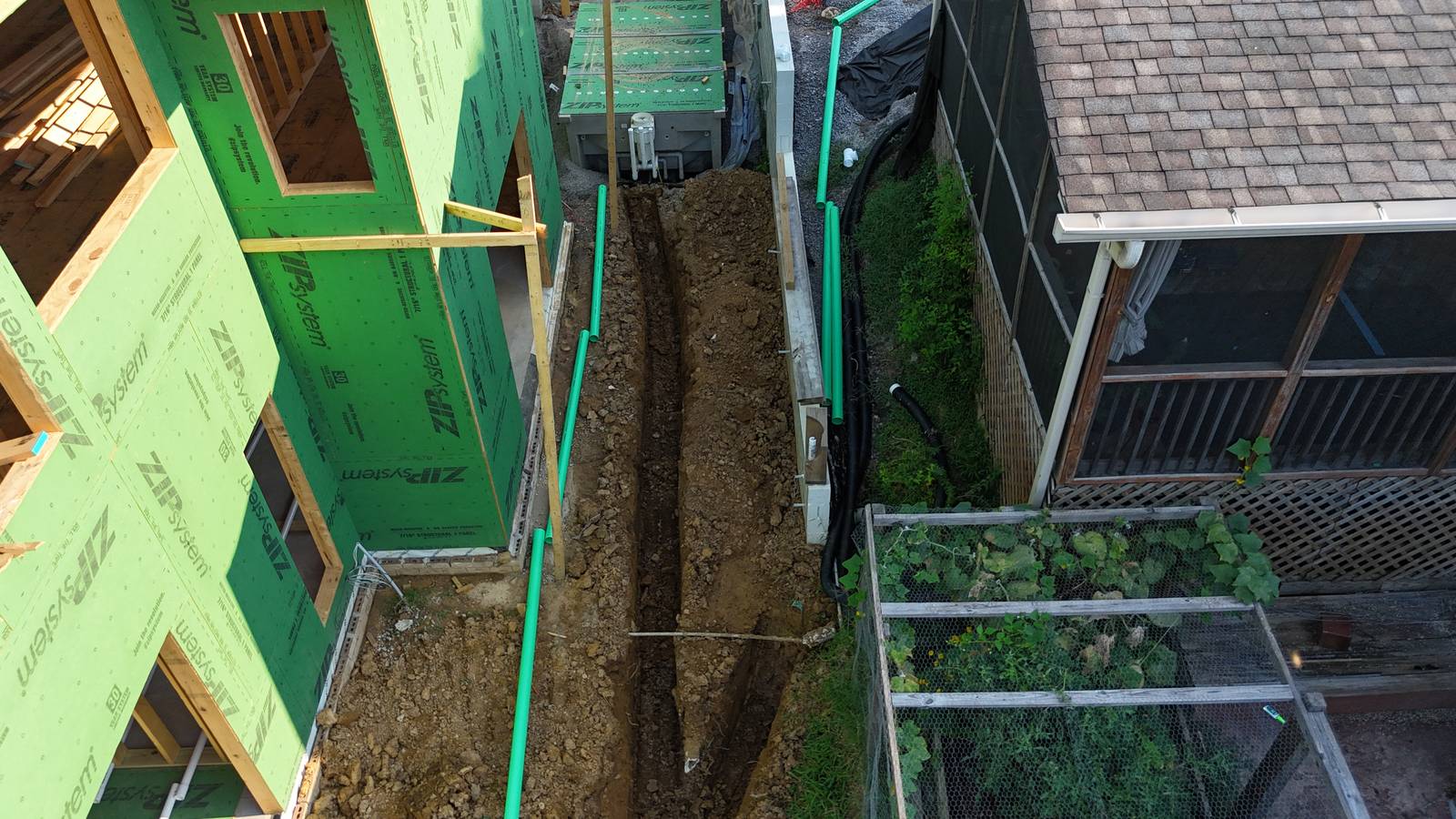Utility trench and green pipe beside a ZIP-sheathed house.